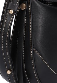 Zwarte leren handtas met contrasterende beige stiksels, een gladde textuur en een opvallend gebogen ontwerp met accenten van goudkleurig beslag.