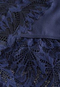 Tessuto blu navy con pizzo intricato a motivo fogliare, che combina superfici lisce e testurizzate in un design elegante.
