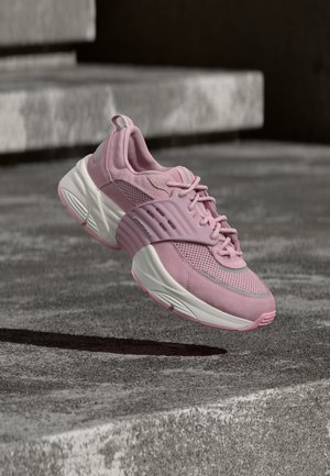 Zapatilla deportiva rosa y blanca con detalles de malla y ante flotando sobre escalones de concreto gris.