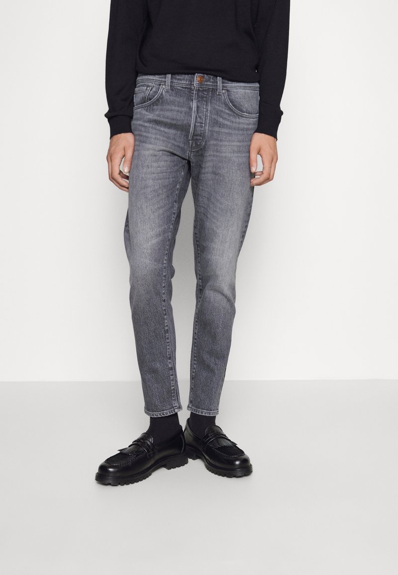 Grå denimjeans med slim fit, femfickorsdesign och blekta detaljer. Kombination med svarta loafers och en svart långärmad topp.