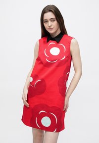 Červené šaty bez rukávov s veľkými kvetinovými vzormi v tmavočervenej a svetlej tyrkysovej farbe, s čiernym golierom a rovnostriehným strihom.