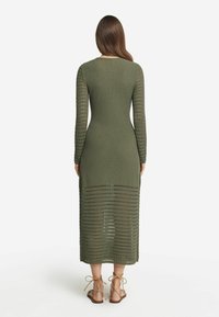 Kläddress i olivgrön med långa ärmar, kroppsnära silhuett och ett strukturerat mönster; nedre delen har horisontella öppna vävningar.