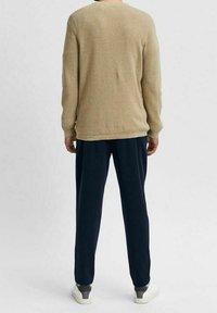 Maglione beige a trama con un taglio rilassato e un collo rotondo, abbinato a pantaloni blu navy morbidi e sneakers bianche.