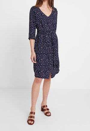 Abito navy con scollo a V, maniche 3/4, cintura regolabile e motivo a pois multicolori; abbinato a sandali con tacco a strappo marroni.