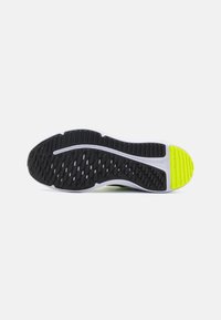 Semelle de chaussure de sport en noir et blanc avec un motif texturé, accentuée d'un caoutchouc jaune vif au niveau du talon et d'une semelle intermédiaire blanche.