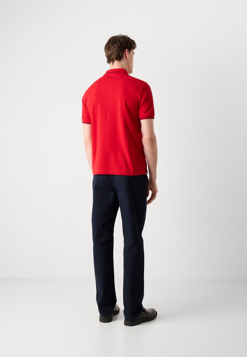 Polo rouge à manches courtes, design ajusté et col côtelé. Assorti à un pantalon droit bleu marine et des chaussures noires.