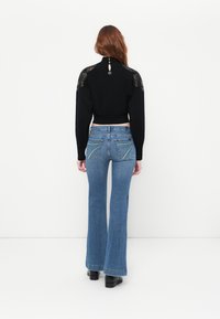 Un pull court noir avec des épaules en dentelle, un jean en denim bleu évasé avec des poches arrière ornées, associé à des bottines noires.