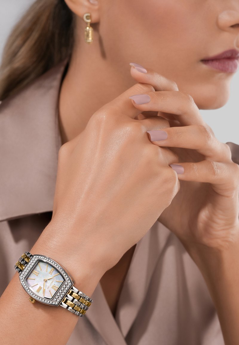 Sölj och guldtonad armbandsur med rektangulärt boett, urtavla i pärlemor, markanta romerska siffror och ett strukturerat armband. Guldaccentsörhängen.