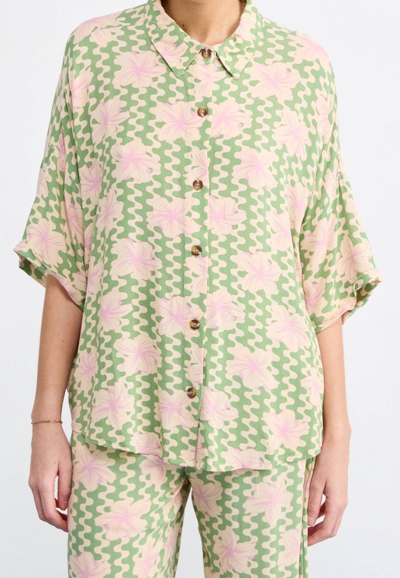 Chemise à manches courtes avec col, en tissu à motif ondulé vert et crème, ornée d'imprimés floraux roses et de boutons en bois.