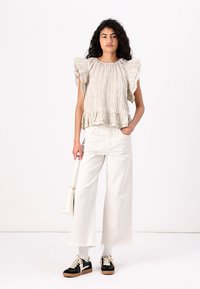 Haut rayé crème et beige avec des manches volantes, associé à un pantalon large blanc et des baskets noires. Modèle tenant un sac à main blanc.