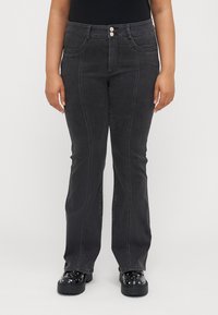 Svarta jeans med vida ben har hög midja, två framfickor och kontrasterande sömmar. Bärs med svarta plattformskor.