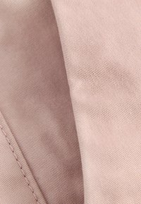 Échantillon de tissu dans une teinte rose doux avec une surface lisse et texturée et des coutures visibles, mettant en avant son pli marqué et son motif tissé.