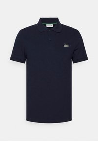 Mörkblå pikétröja i bomull; har en klassisk krage, två knappar och en liten grön krokodil-logotyp på vänster bröst.