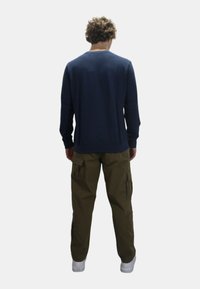 Camicia a maniche lunghe navy abbinata a pantaloni cargo color oliva. La camicia presenta un collo rotondo; i pantaloni hanno tasche laterali e una vestibilità comoda.