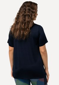 Top corto blu navy con un motivo textured, caratterizzato da una vestibilità rilassata e un orlo arrotondato. Indossato sopra leggings multicolore con motivo.