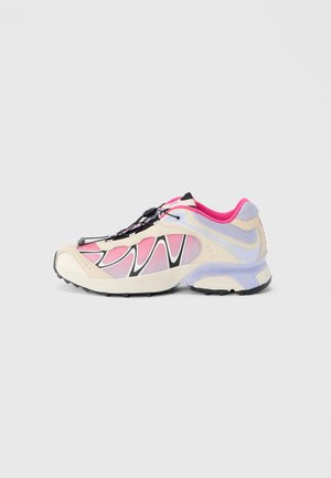 Chaussure de sport à base crème, motifs ondulés rose et noir, dessus en mesh, lacets élastiques, et une semelle en caoutchouc noire avec un accent violet clair.