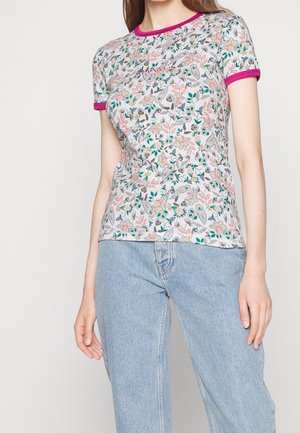 Kvinde iført en tætsiddende kortærmet blomstret top med lyserød kant, kombineret med lyseblå højtaljede jeans.