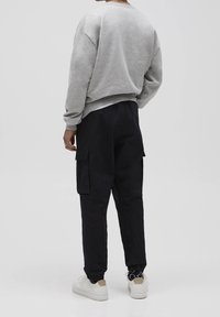 Szary sweter z bawełnianej mieszanki, luźny krój. Czarne spodnie cargo z kieszeniami, zaciągane przy nogawkach. Białe trampki z beżowymi akcentami.