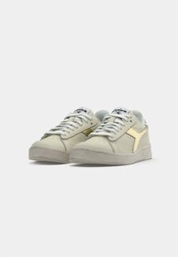 Light green sneakers with a textured finish, white laces, gold accents on the side, and a rubber sole. Branding on the tongue.