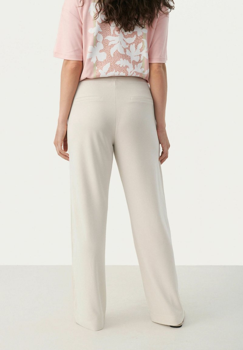 Helle beigefarbene, weit geschnittene Hosen aus einem glatten Material mit Gesäßtaschen, kombiniert mit einem rosa T-Shirt mit kurzen Ärmeln, das ein florales Muster aufweist.