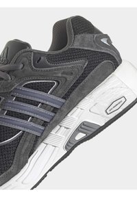 Melnas un pelēkas sporta kedas ar sietveida augšdaļu, ādas akcentiem, trim pelēkām svītrām, baltu vidusdaļu un teksturētu gumijas zoli.