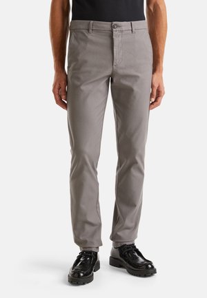 Pantaloni grigi in cotone con vestibilità regolare, dotati di zip e chiusura con bottone. Abbinati a scarpe eleganti nere lucide.