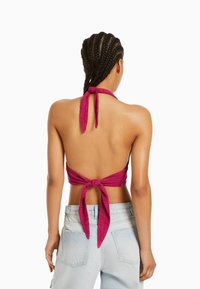 Magenta halterneck-topp med knytning bak, tillverkad av lätt tyg, kombinerad med ljusblå högmidjade jeans.