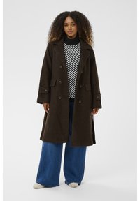 Bruine wollen gemengde dubbelgeknoopte jas met grote voorzakken, reverskraag en knoopaccenten, gecombineerd met een gestreepte trui en wijde jeans.