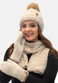 Bonnet en tricot beige avec un pompon, écharpe et gants assortis, présentant des motifs texturés et des poignets côtelés.
