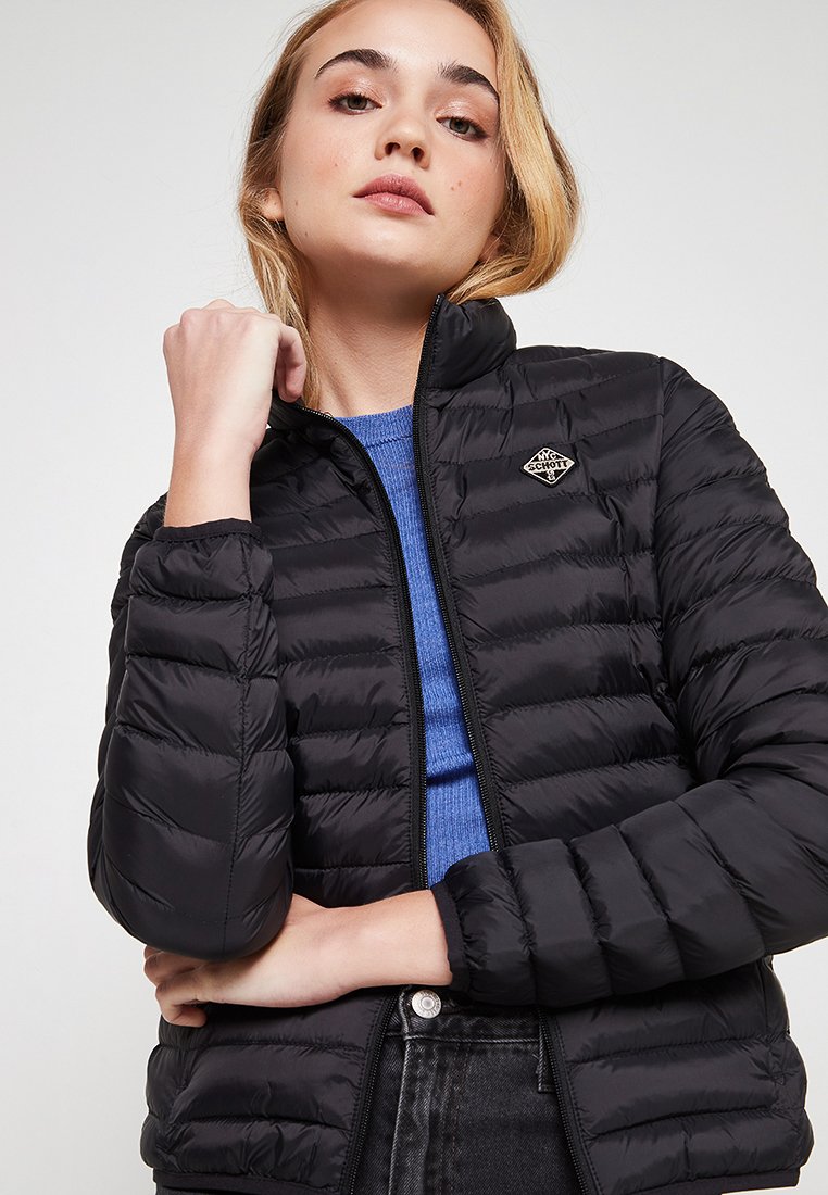 Veste polaire noire avec fermeture éclair à l'avant, coutures horizontales, col haut et un petit logo sur la poitrine gauche. Portée sur un haut bleu.