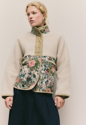 Fleece and floral jacket featuring a beige upper, vibrant floral lower with pink blooms, coordinating green trim, and snap button closure.
