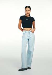 Czarny krótkotrwały t-shirt z haftem "Rêverie", jasnoniebieskie szerokie dżinsy i czarne płaskie buty z ćwiekami, na jednolitym białym tle.