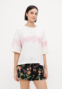 Witte katoenen T-shirt met een roze bloemenprint op de borst, korte mouwen en een losse pasvorm. Gepaard met zwarte shorts met een kleurrijk bloemenpatroon.