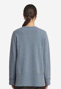 Jasnoniebieski sweter robiony na drutach z prążkowanymi mankietami i dołem. Posiada luźny krój oraz okrągły dekolt, a także miękką fakturę.