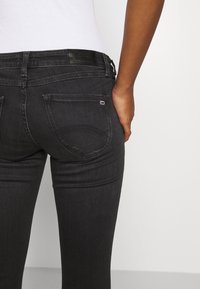 Black denim jeans with a fitted design, featuring two back pockets and a leather label at the waist. The fabric has a smooth texture.