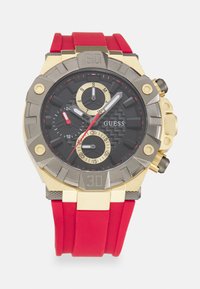 Schwarze Chronographuhr mit goldenen Akzenten und einem roten Gummiband. Sie verfügt über drei Zifferblätter, ein strukturiertes Zifferblatt und große arabische Ziffern.