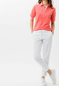 Korálová polo košile s límečkem a knoflíkovou légou, kombinovaná s bílými kalhotami na míru a bílými teniskami. Jednoduchý, čistý design.