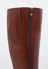 Bota hasta la rodilla de cuero marrón con cierre de cremallera en el lateral y diseño partido en la parte superior. Textura suave y acabado pulido.