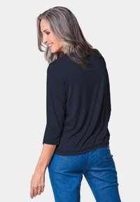 Marineblaues, leichtes Oberteil mit Rundhalsausschnitt und Dreiviertelärmeln, das einen gerafften Saum und eine glatte Textur aufweist, kombiniert mit blauen Jeans.