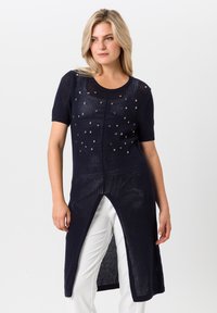 Marineblauwe gebreide tuniek met korte mouwen, voorzien van decoratieve uitsparingen en een hoge split aan de voorkant. Lichtgewicht en ademende stof.