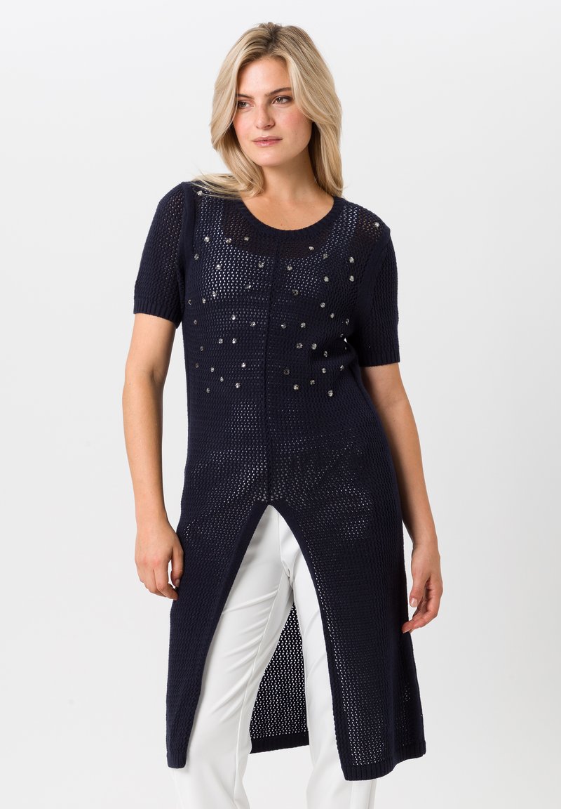 Marineblauwe gebreide tuniek met korte mouwen, voorzien van decoratieve uitsparingen en een hoge split aan de voorkant. Lichtgewicht en ademende stof.