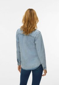 Camicia di jeans azzurro chiaro con maniche lunghe, orlo arrotondato e polsini con bottoni. Il tessuto presenta un aspetto sbiadito e strutturato.