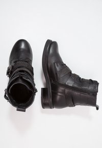 Las botas de cuero negras hasta el tobillo cuentan con una puntera redondeada, correas decorativas con tachuelas, acentos texturizados y una cremallera lateral para facilitar su uso.