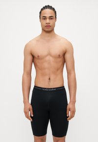 Pantalones cortos atléticos negros con cintura elástica, con el nombre de la marca "icebreaker" en gris. Textura suave y diseño ajustado.