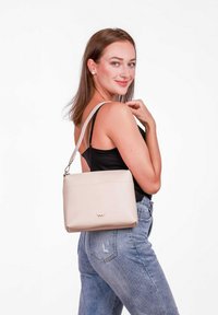 Béžová kabelka přes rameno z hladkého materiálu, s horním zipem a zlatým logem. Velikost se jeví jako střední, jednoduchý obdélníkový tvar.