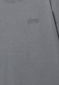 Grå crew-neck t-shirt lavet af blød bomuld, med et diskret broderet logo på brystet og en glat tekstur i hele stoffet.