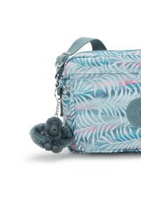 Borsa azzurra chiara con motivo di foglie di palma in verde e rosa. Presenta una tasca con zip, una tracolla grigia e un portachiavi a forma di gorilla peloso grigio.