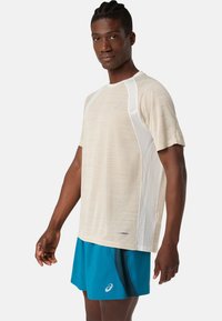 T-shirt de sport beige avec un tissu texturé et des panneaux latéraux blancs, associé à un short turquoise arborant un logo et des accents contrastants.