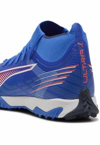 Zapatilla deportiva azul con parte superior de malla texturizada, acentos rojos en contraste y una entresuela blanca. Cuenta con un collar alto y suela con tracción.