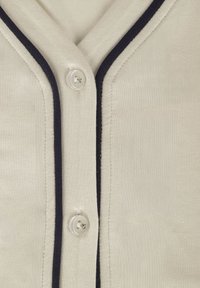 Közeli kép bézs színű anyagról fekete szegéllyel, amelyen két áttetsző gomb látható, fehér cérnával varrva.